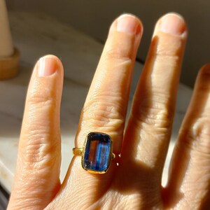 May include: A gold ring featuring a large, rectangular, blue gemstone. The ring's band is a simple, polished gold. The gemstone is a deep, vibrant blue, with a rectangular cut. The ring is worn on a finger.