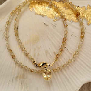 Peut inclure: Un collier composé de petites perles jaunes translucides et facettées disposées en cercle. Le collier présente un pendentif unique en pierre jaune de forme ovale à la base et est fixé par un fermoir mousqueton en métal doré.