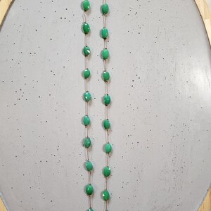 May include: A delicate necklace featuring oval-shaped, light green beads strung on a thin, gold-colored chain. The beads are evenly spaced, creating a simple yet elegant design. The necklace is displayed on a light gray surface.