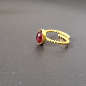 Puede incluir: Un anillo de oro con una piedra preciosa roja. El anillo est&aacute; hecho de alambre retorcido.