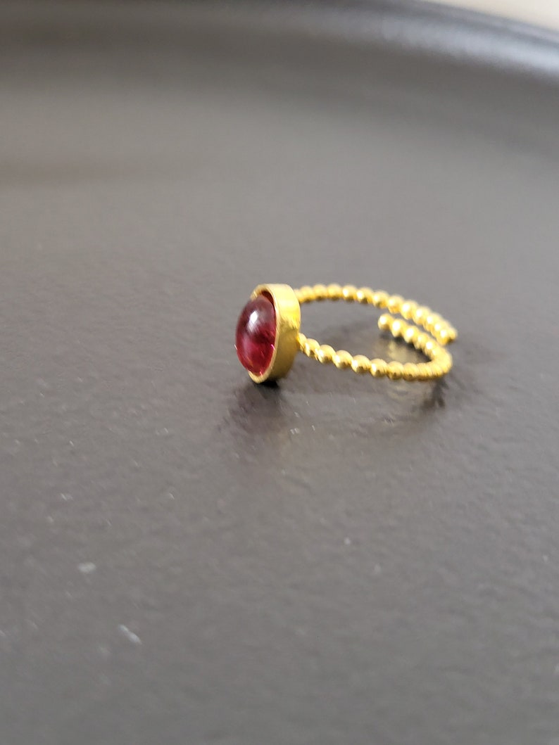 Puede incluir: Un anillo de oro con una piedra preciosa roja. El anillo est&aacute; hecho de alambre retorcido.