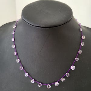 Op de afbeelding: Een paarse ketting met kleine, lichtpaarse edelsteen kralen. De ketting is geregen op een dun paars koord.