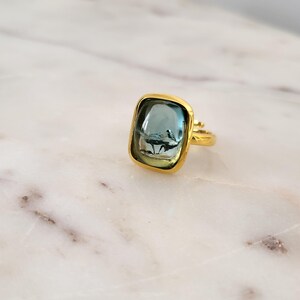 May include: A gold ring with a square-shaped blue gemstone. The ring is set in a gold band.