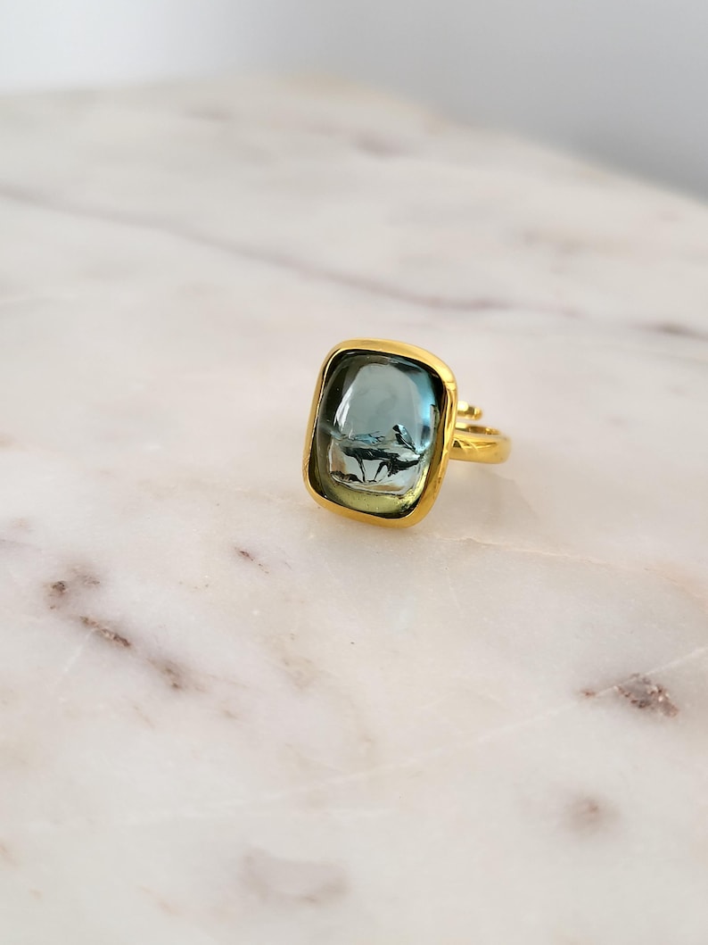 May include: A gold ring with a square-shaped blue gemstone. The ring is set in a gold band.