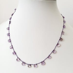 Op de afbeelding: Een delicate ketting met een paarse koord en kleine, lichtpaarse edelsteen kralen.