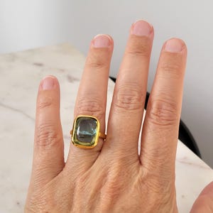 May include: A gold ring with a large, rectangular, green and blue gemstone.