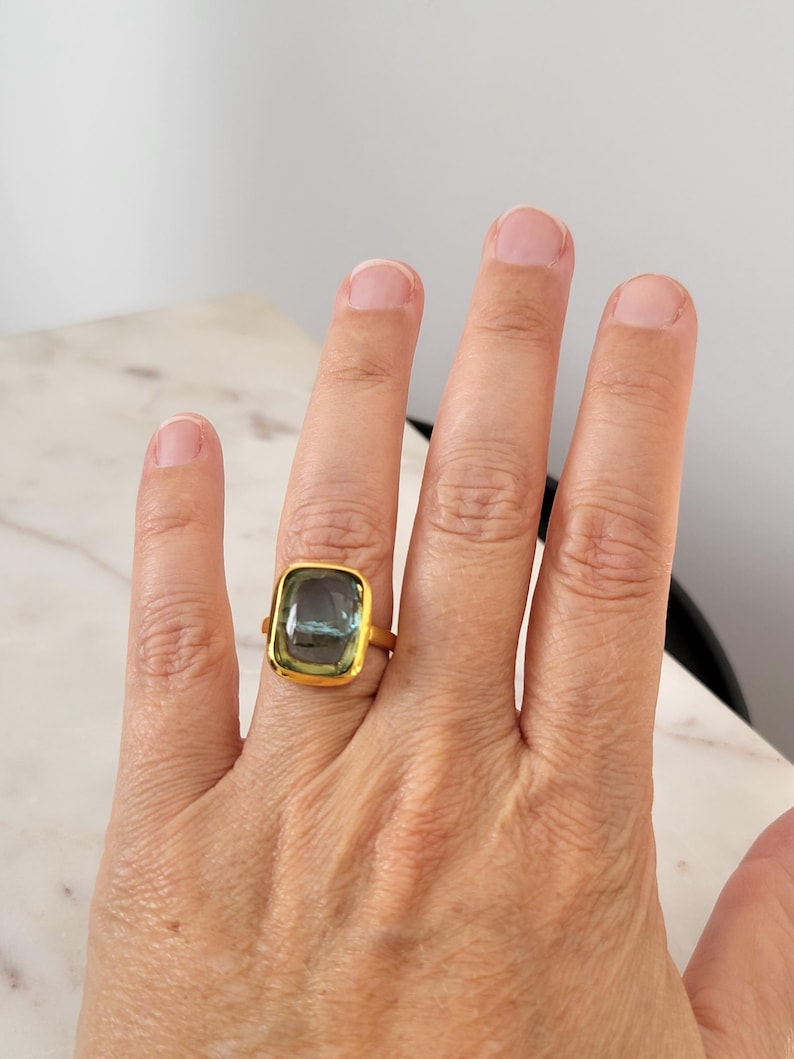 May include: A gold ring with a large, rectangular, green and blue gemstone.