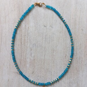 May include: A turquoise blue beaded necklace with a gold pendant featuring a turquoise stone. The necklace is made of small, round beads and has a simple, elegant design.