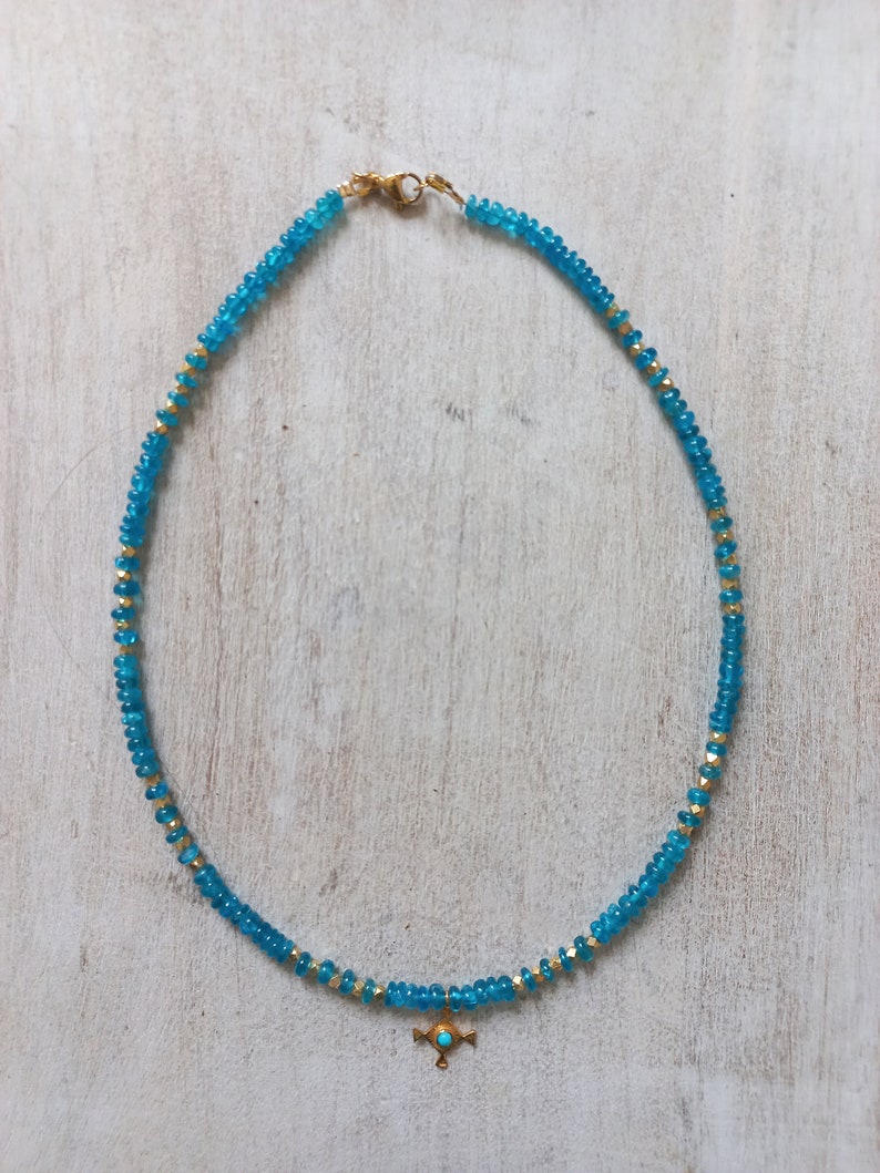 May include: A turquoise blue beaded necklace with a gold pendant featuring a turquoise stone. The necklace is made of small, round beads and has a simple, elegant design.