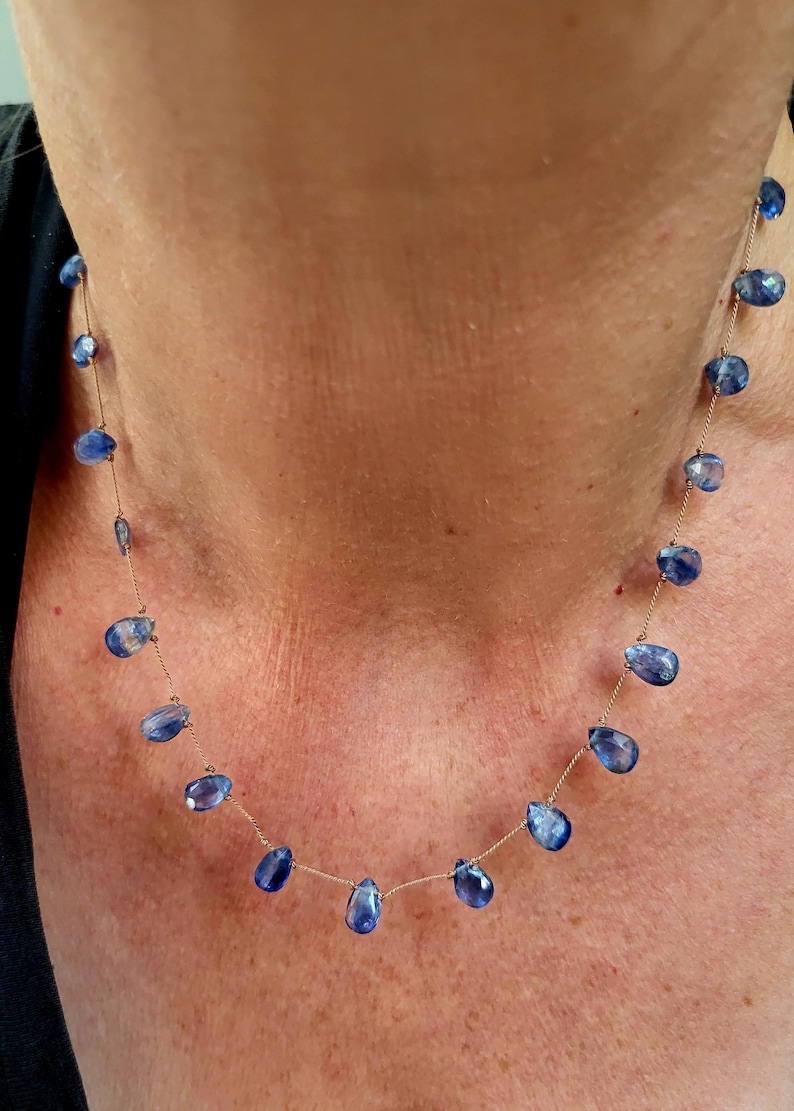 Puede incluir: Un collar delicado que presenta una cadena dorada fina intercalada con m&uacute;ltiples piedras preciosas azules peque&ntilde;as, facetadas y con forma de l&aacute;grima. Las piedras est&aacute;n espaciadas uniformemente a lo largo de la cadena, creando un efecto flotante.