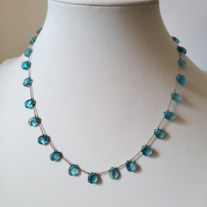 Pu&ograve; includere: Una delicata collana con perline a forma di goccia, di colore azzurro chiaro, infilate su una sottile catena marrone. Le perline sono distanziate in modo uniforme, creando un design minimalista ed elegante. La collana &egrave; esposta su un manichino bianco.