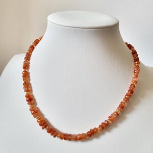 Peut inclure: Un collier compos&eacute; de petites perles orange-rouge &agrave; facettes. Les perles sont enfil&eacute;es pour former une forme circulaire, pr&eacute;sent&eacute; sur un mannequin blanc. Le collier a une tonalit&eacute; chaude et terreuse.