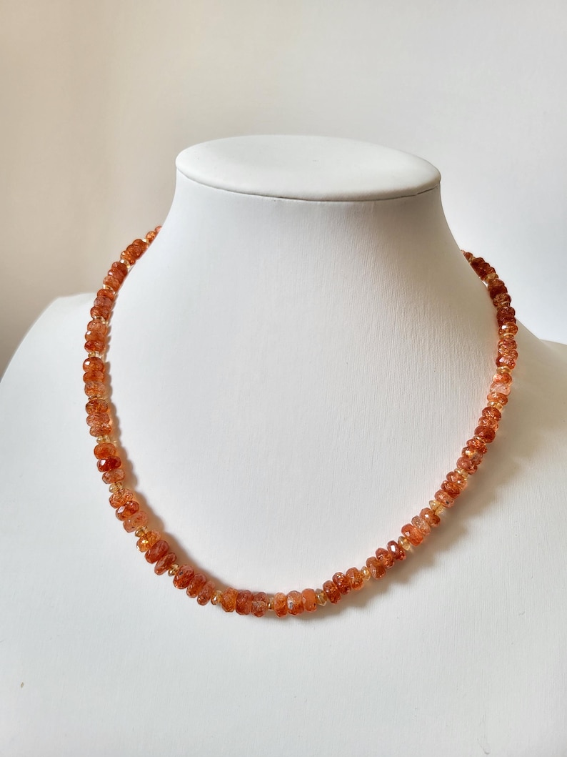 Peut inclure: Un collier compos&eacute; de petites perles orange-rouge &agrave; facettes. Les perles sont enfil&eacute;es pour former une forme circulaire, pr&eacute;sent&eacute; sur un mannequin blanc. Le collier a une tonalit&eacute; chaude et terreuse.