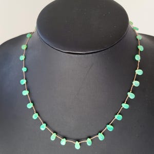 Pode incluir: Um colar delicado feito com contas verde claro em forma de l&aacute;grima enfiadas em uma fina corrente dourada.