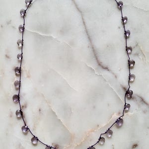 Op de afbeelding: Een delicate ketting met een paars koord en kleine, heldere, gefacetteerde amethist kralen.