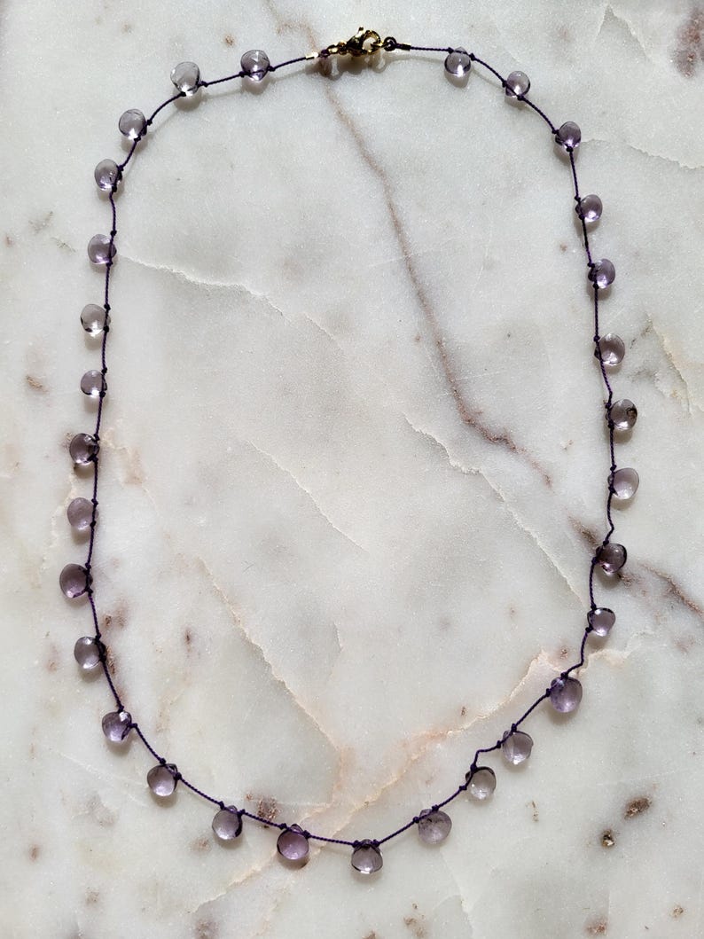 Op de afbeelding: Een delicate ketting met een paars koord en kleine, heldere, gefacetteerde amethist kralen.