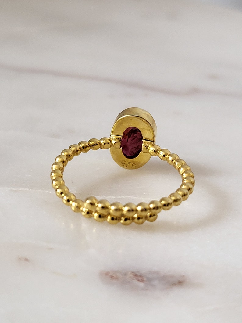 Puede incluir: Un anillo de oro con una banda retorcida y una piedra ovalada roja. El anillo est&aacute; marcado con el n&uacute;mero "925".