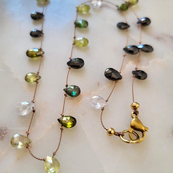 A delicate, minimalist necklace featuring natural green, yellow, and white zircon stones on a brown silk thread.