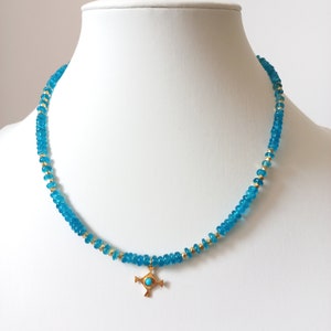 May include: A turquoise blue beaded necklace with a gold cross pendant. The cross has a turquoise blue stone in the center.