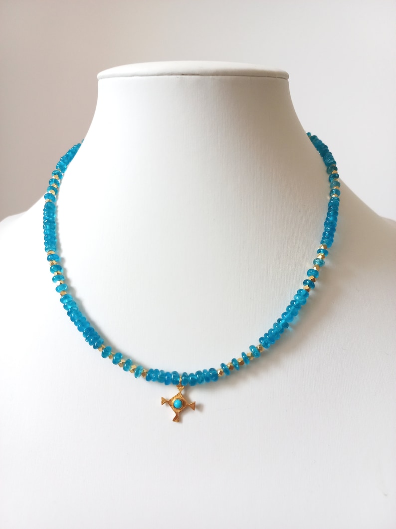 May include: A turquoise blue beaded necklace with a gold cross pendant. The cross has a turquoise blue stone in the center.