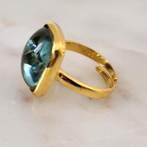 May include: Gold ring with a large, square-shaped, blue gemstone.