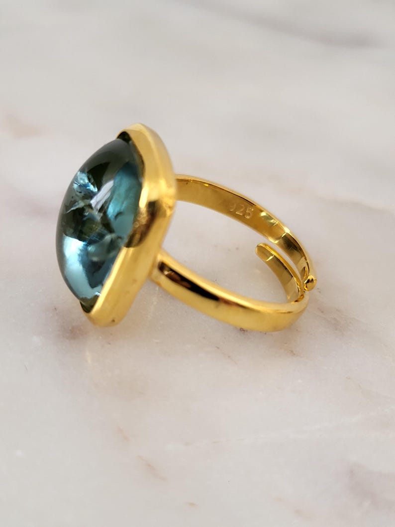 May include: Gold ring with a large, square-shaped, blue gemstone.