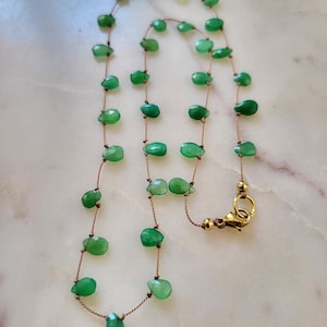 May include: A delicate necklace featuring faceted, teardrop-shaped green gemstones strung on a thin, brown cord. The necklace has a gold-colored clasp. The gemstones are evenly spaced along the cord, creating a simple yet elegant design.