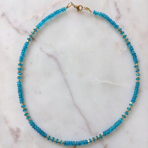 May include: A turquoise blue and gold beaded necklace with a small turquoise cross pendant.