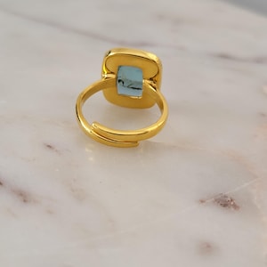 May include: A gold ring with a light blue square-shaped stone set in the center.