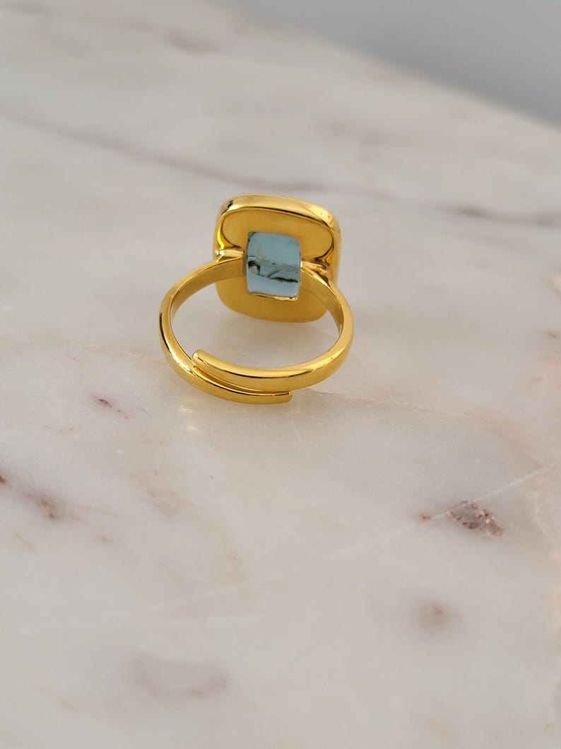 May include: A gold ring with a light blue square-shaped stone set in the center.