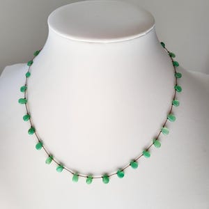 Pode incluir: Um delicado colar de pedras preciosas verdes com um cord&atilde;o marrom. O colar apresenta pequenas pedras preciosas de forma oval enfiadas em um cord&atilde;o fino.