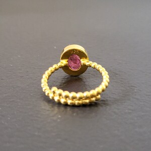 May include: A gold ring with a pink oval gemstone. The ring is made of a twisted band of small gold beads. The back of the ring is stamped with "925".