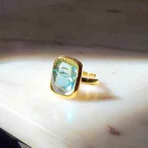 May include: A gold ring with a light blue and green rectangular gemstone.