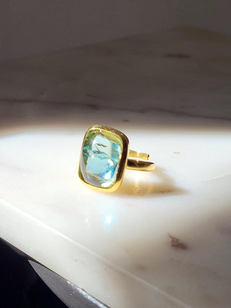 May include: A gold ring with a light blue and green rectangular gemstone.