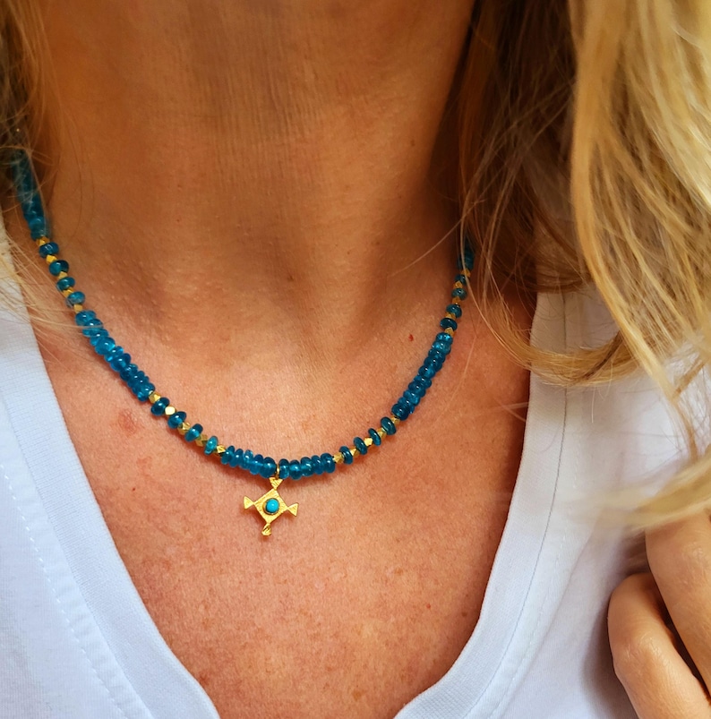 May include: A gold necklace with a turquoise cross pendant. The necklace is made of small, round, blue beads.