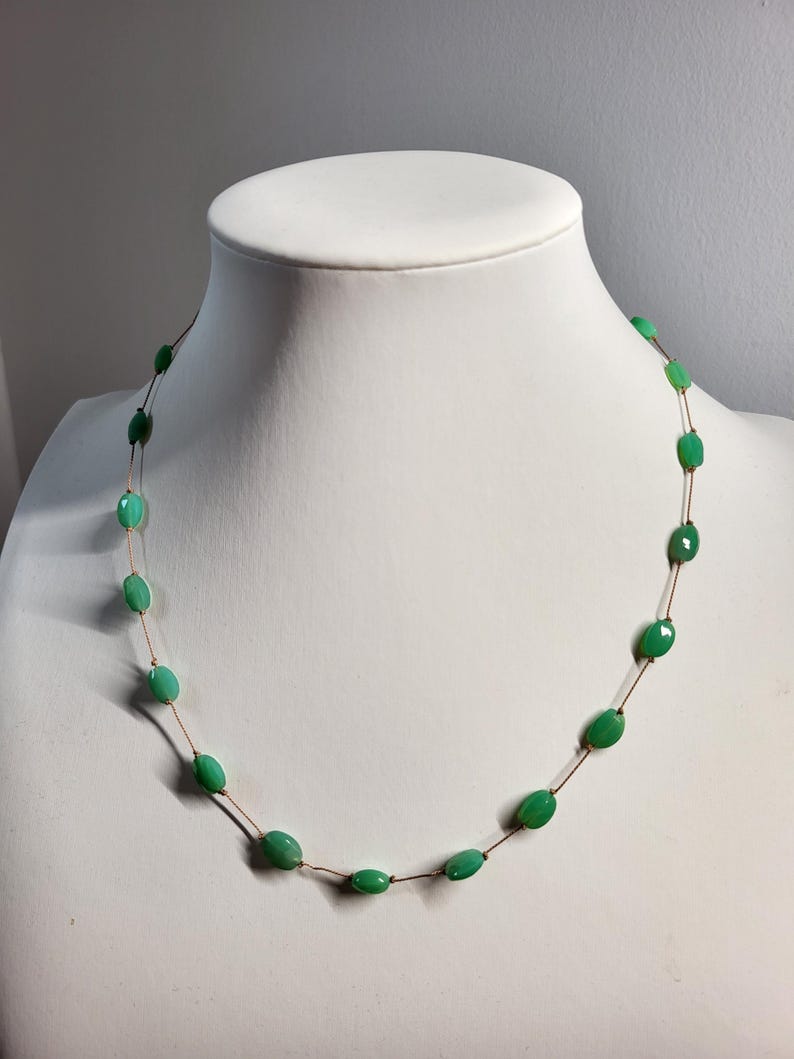 May include: A delicate necklace featuring oval-shaped, bright green beads strung on a thin, brown cord. The beads are evenly spaced, creating a minimalist and elegant design. The necklace is displayed on a white mannequin bust.