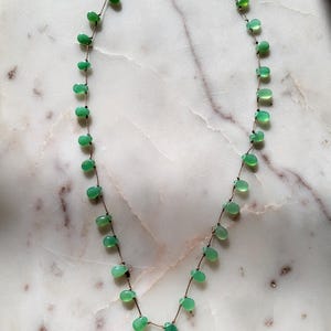 Pode incluir: Um delicado colar de corrente de ouro com uma s&eacute;rie de pequenas pedras preciosas verdes em forma de l&aacute;grima.