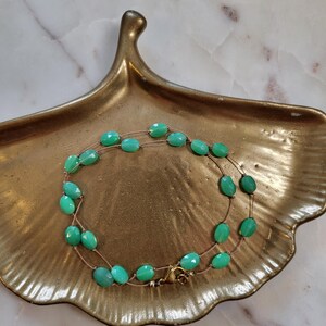 May include: A double-strand necklace featuring oval, faceted, turquoise-colored beads. The beads are strung on a delicate, gold-toned chain. The necklace is displayed on a gold-colored, leaf-shaped dish.