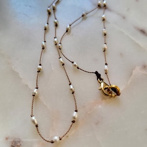 A pretty, lustery white pearl necklace on a brown silk thread; a delicate, minimalist, fine necklace.