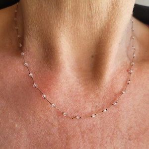 May include: Delicate necklace featuring small, clear beads strung on a thin, gold-colored chain. The necklace is displayed against a skin tone background, highlighting the minimalist design. A simple and elegant piece of jewelry.