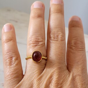 May include: A gold ring with a dark red oval gemstone set in a beaded band.