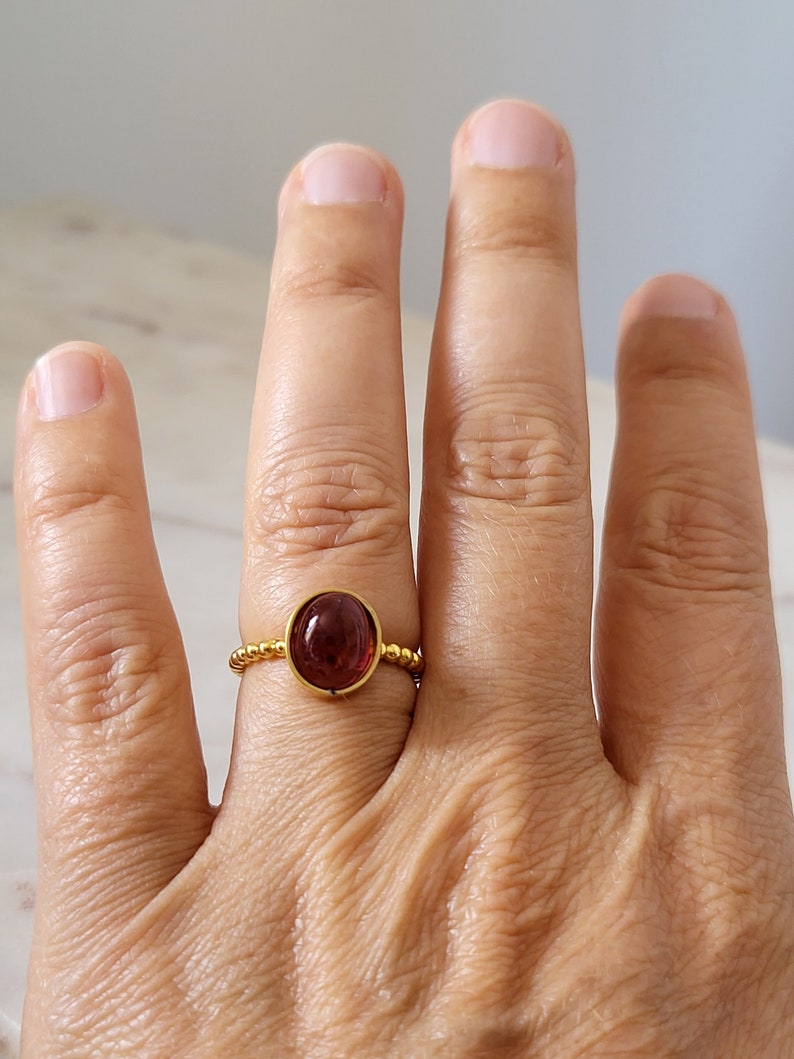 May include: A gold ring with a dark red oval gemstone set in a beaded band.
