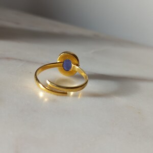 K&ouml;nnte beinhalten: Ein goldener Ring mit einem blauen, ovalen Stein in der Mitte. Der Ring ist offen und verstellbar.