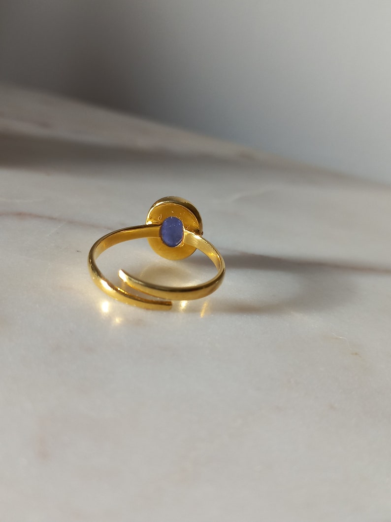 K&ouml;nnte beinhalten: Ein goldener Ring mit einem blauen, ovalen Stein in der Mitte. Der Ring ist offen und verstellbar.