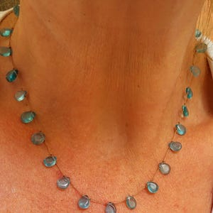 Pu&ograve; includere: Delicata collana con pietre preziose blu a forma di goccia infilate su una sottile catena color oro. La collana &egrave; esposta su uno sfondo neutro, evidenziando il blu vibrante delle pietre.
