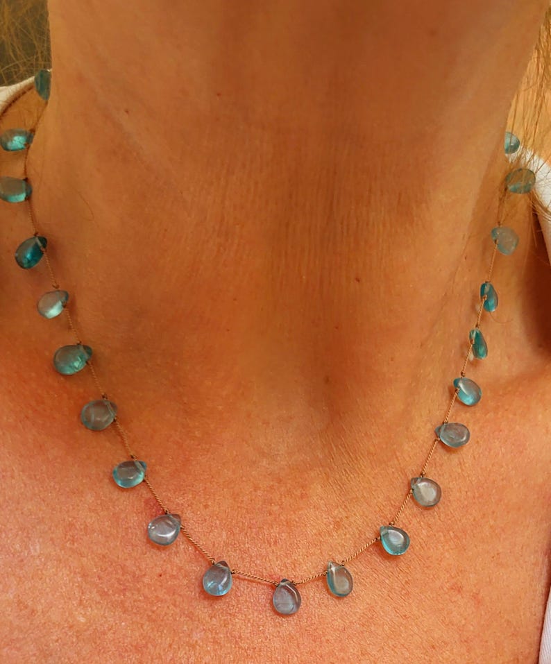 Pu&ograve; includere: Delicata collana con pietre preziose blu a forma di goccia infilate su una sottile catena color oro. La collana &egrave; esposta su uno sfondo neutro, evidenziando il blu vibrante delle pietre.