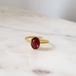 Puede incluir: Un anillo de oro con una piedra ovalada roja. El anillo est&aacute; hecho de peque&ntilde;as cuentas doradas.
