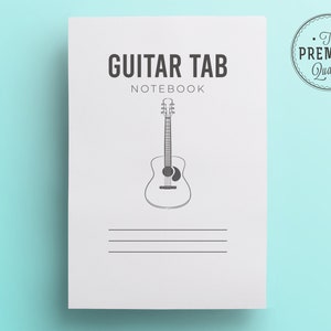 May include: A white Guitar Tab Notebook with a black line drawing of an acoustic guitar. The notebook has the words "GUITAR TAB NOTEBOOK" printed in black. A circular "The Premium Quality" seal is in the upper right corner.