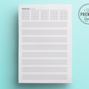 May include: A white Guitar Tab Notebook with a light blue background. The notebook features guitar tab diagrams at the top and horizontal lines for musical notation. The text "GUITAR TAB NOTEBOOK" is at the top, and a circular "The Premium Quality" seal is in the upper right corner.