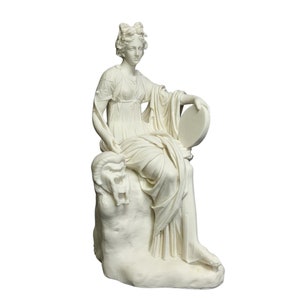 May include: A white sculpture of a seated woman in classical attire, holding a circular object. The figure rests on a textured base with a ram's head carved into it. The statue has intricate details and is set against a white background.
